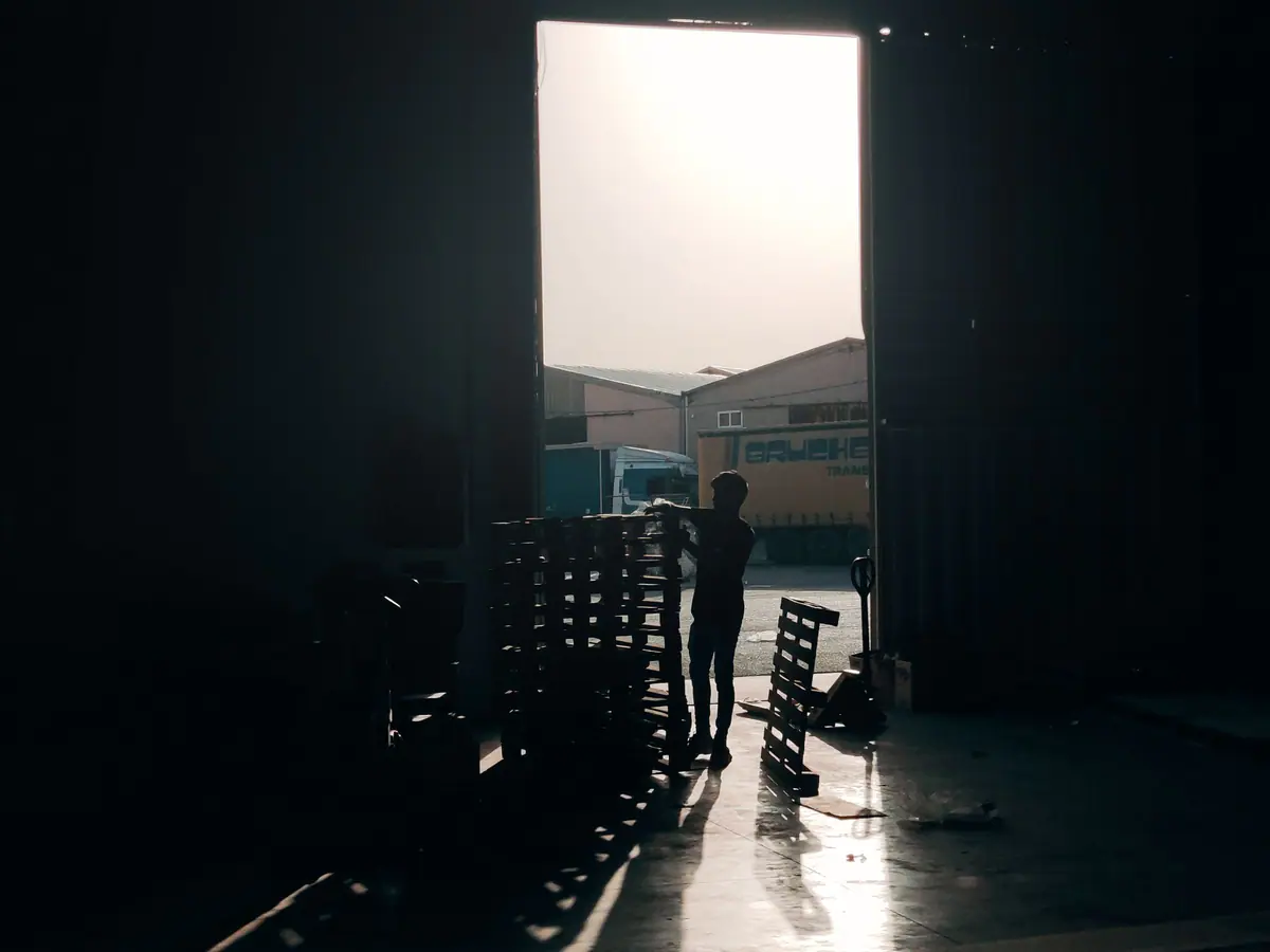 A worker silhouetted in a warehouse doorway beside stacked pallets
